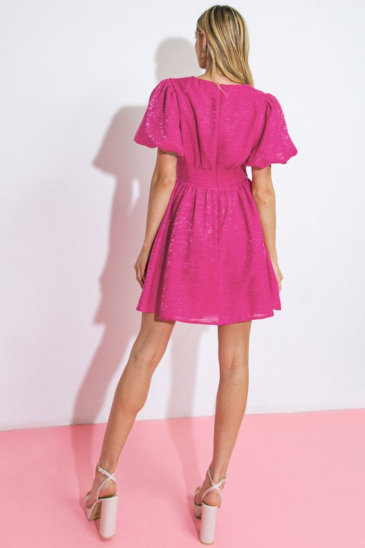 A textured woven mini dress featuring surplice neckline, short puff sleeve, full skirt and back zipper closure